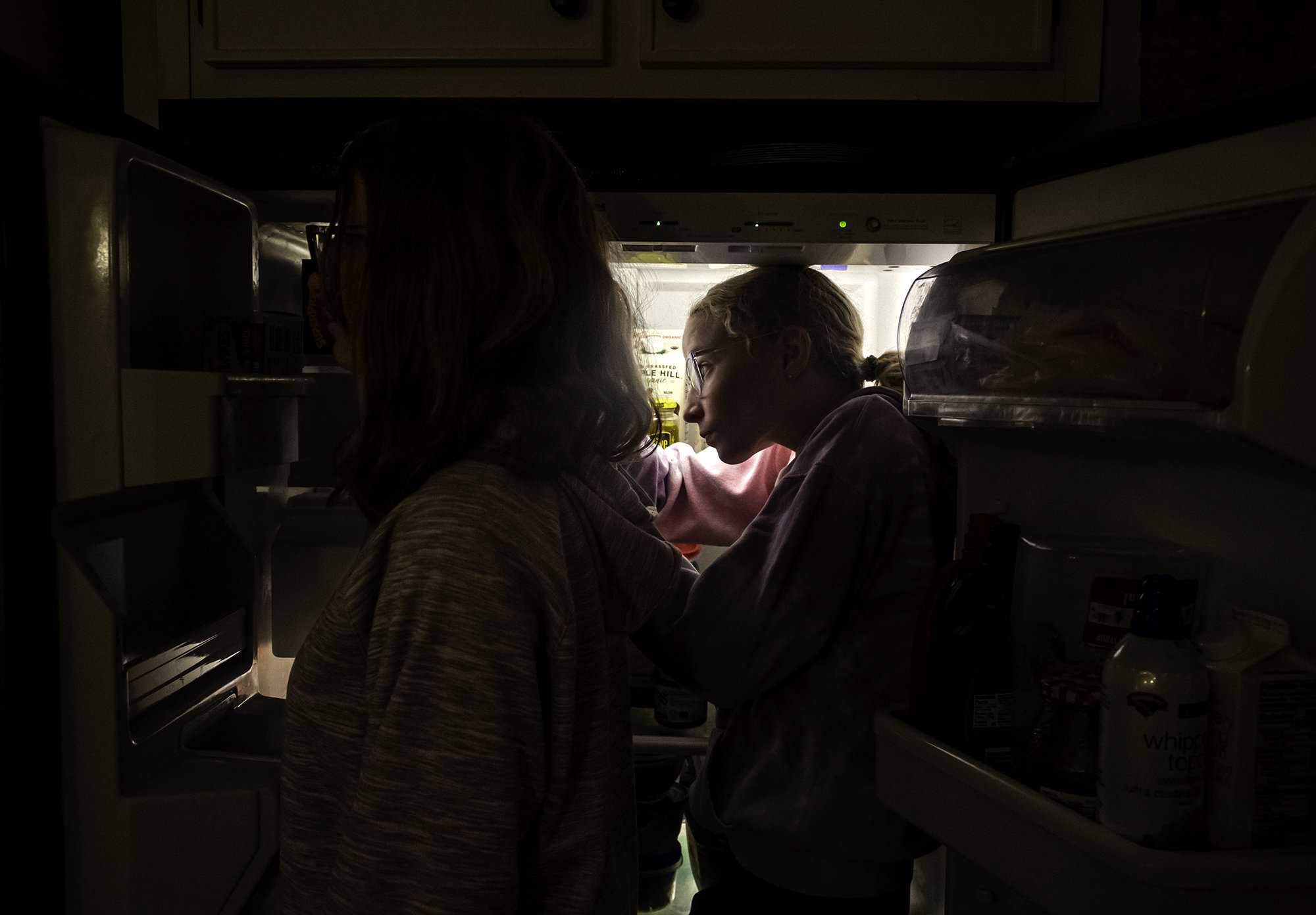Picture of two young women standing between the open doors of a refrigerator.