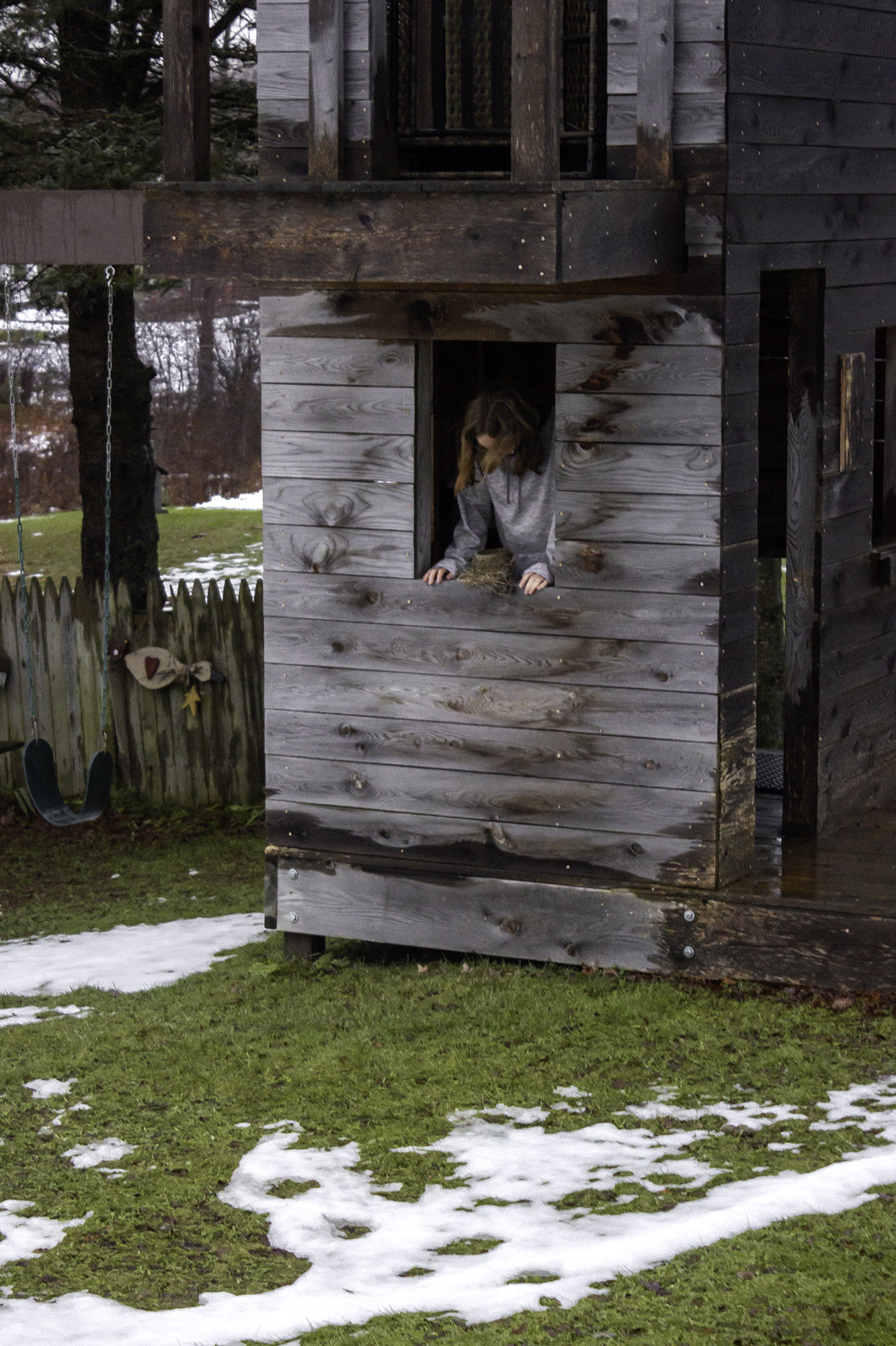 Picture of a young woman looking out from a wooden structure into the melting snow.