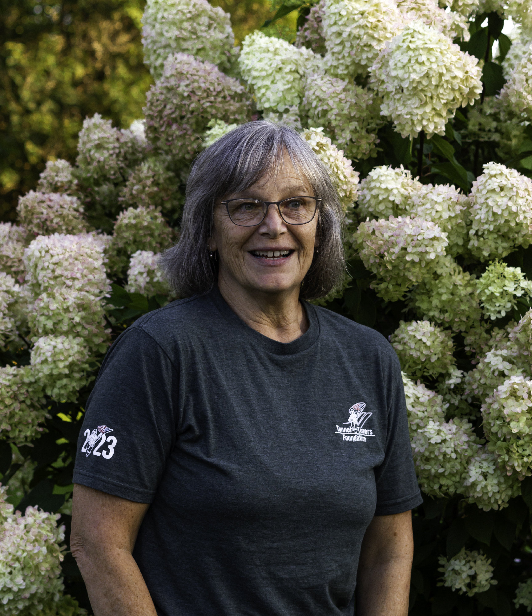 Portrait of an older lady in front of a hydrangea plant.