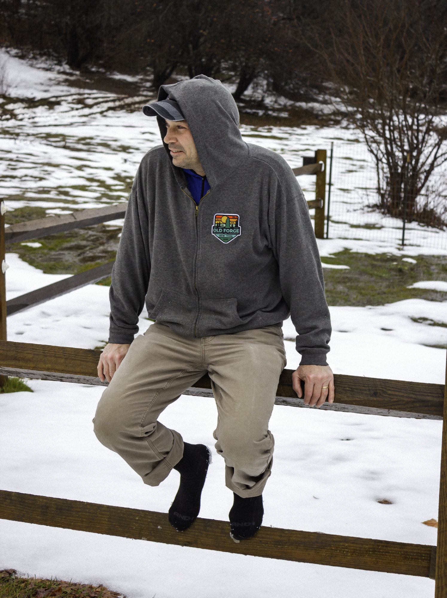 Portrait of a man sitting on a fence wearing socks in the middle of winter.