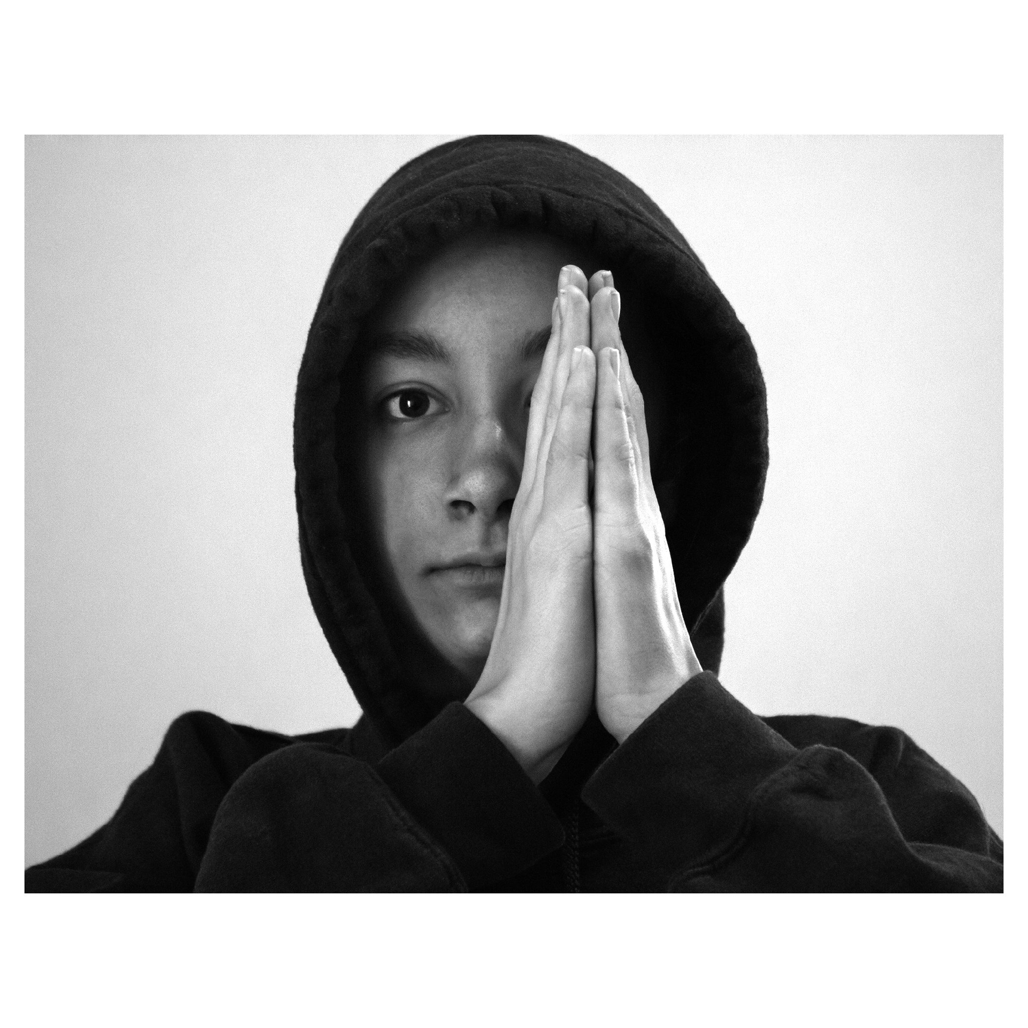 Portrait of a young lady with a hooded sweatshirt hiding half of her face with praying hands.
