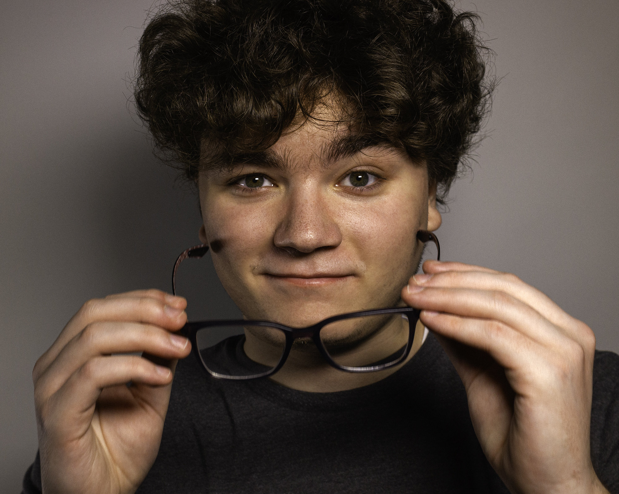 Portrait of Jacob Healt raising his eyebrows while holding his glasses away from his face.